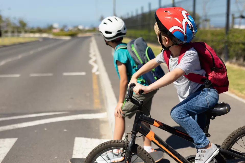Two young boys wearing bike helmets looking right before crossing the street on their bicycles